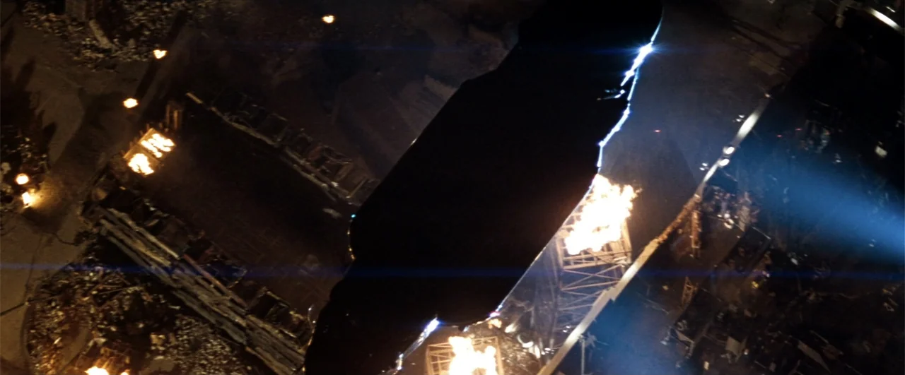 Demolition Man (1993) movie still: establishing — A nighttime aerial view of a dark wreckage site filled with scattered metal debris. Several small…