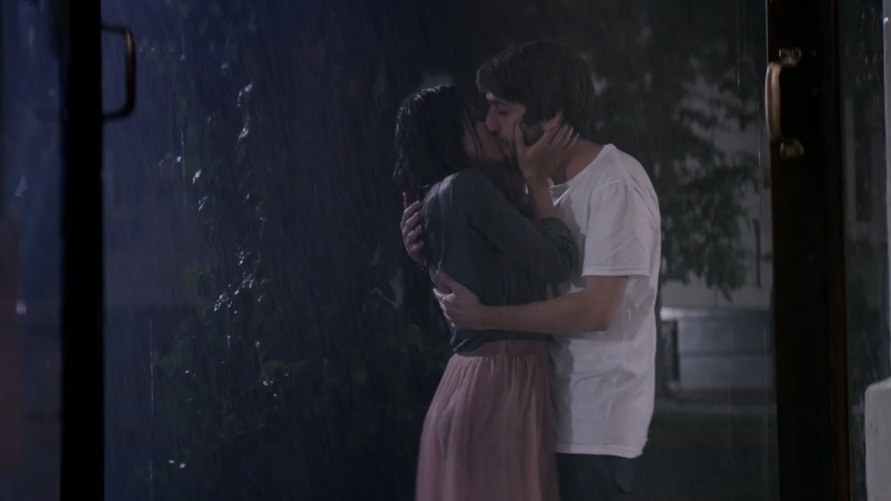 That's Not Cheating (2016) movie still: medium — A dark outdoor space during a rainstorm at night with visible water streaks. A young man and woman…