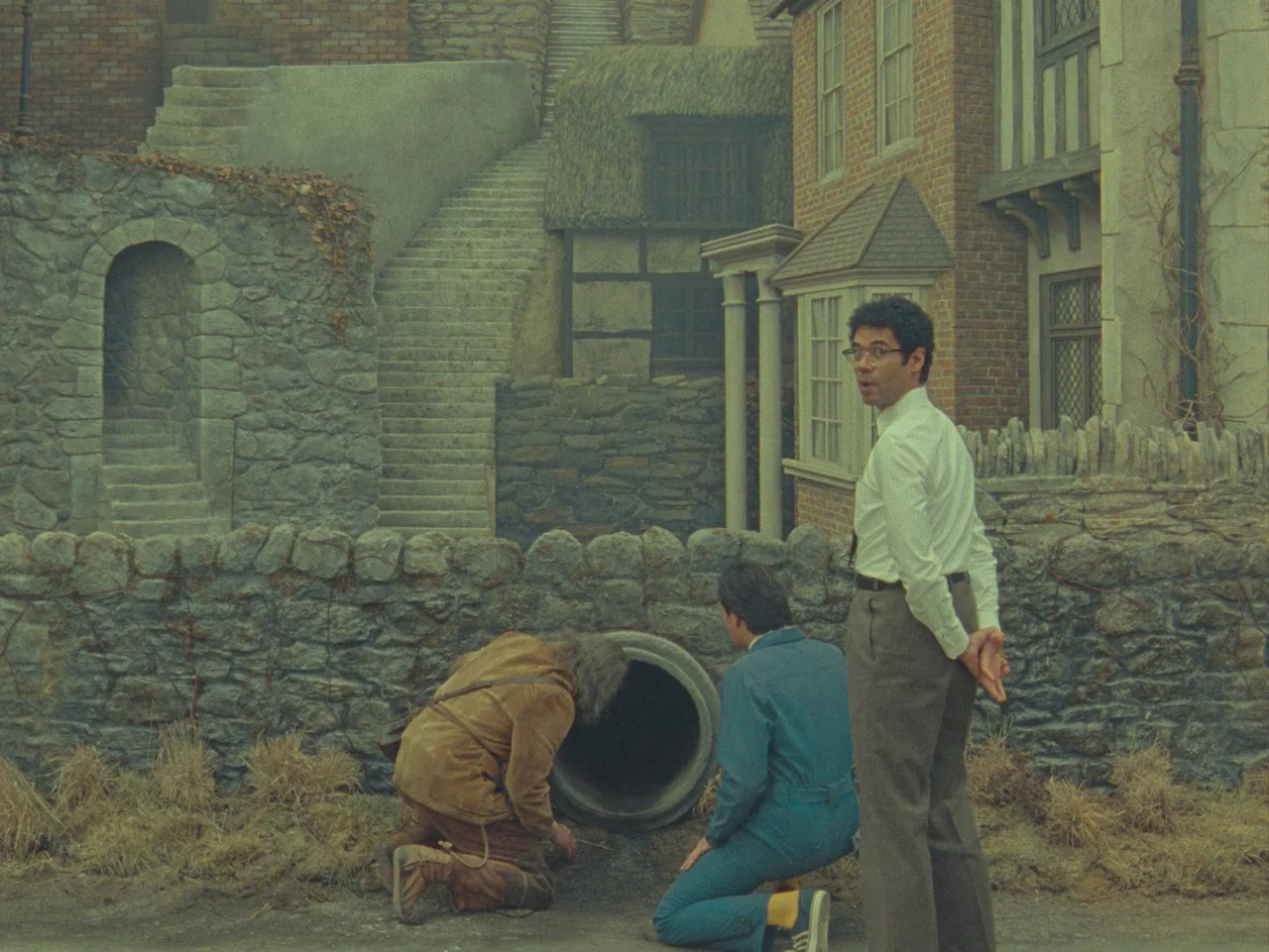 The Rat Catcher (2023) movie still: medium — A miniature-style set depicts a small stone village with quaint houses and staircases. Three men in…