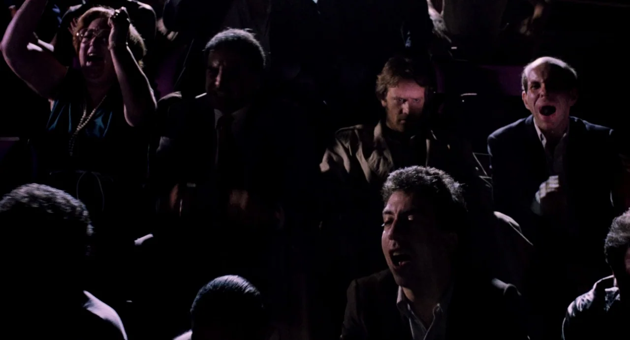 Highlander (1986) movie still: medium — A group of people sit in a dark room illuminated by screen light. The individuals react with expressions of…