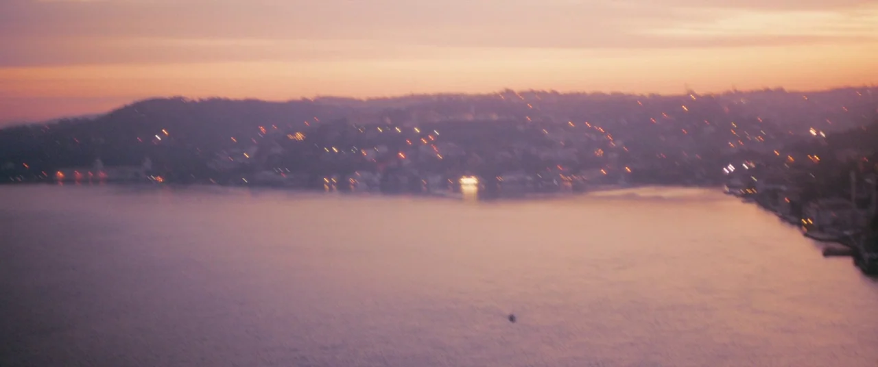 Mustang (2015) movie still: establishing — A wide view of a large body of water during the late twilight hours. Distant buildings along the…
