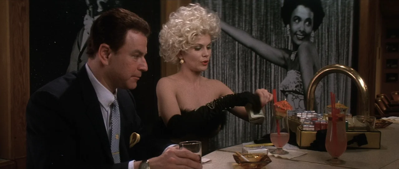 Cobb (1994) movie still: medium — A dimly lit lounge setting features a bar counter with cocktails and cigarette packs. A man in a suit sits with a…
