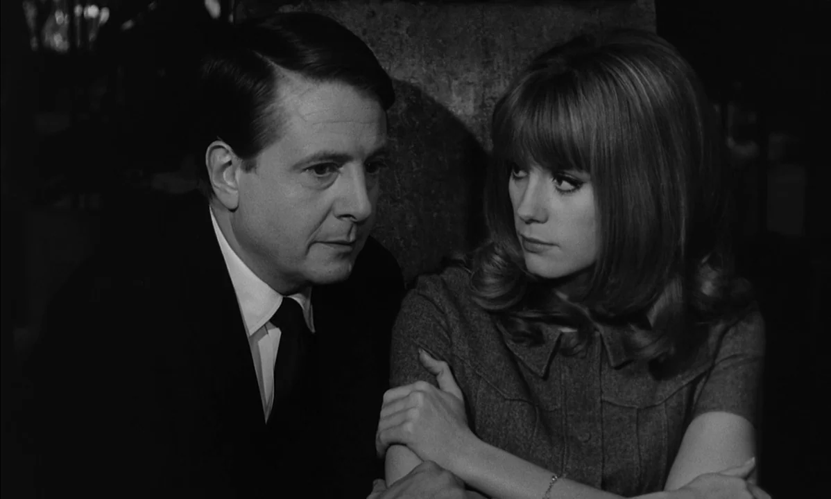 La Peau Douce (The Soft Skin) (1964) movie still: medium — A dark indoor space where two people sit close to one another. The man in a suit looks…