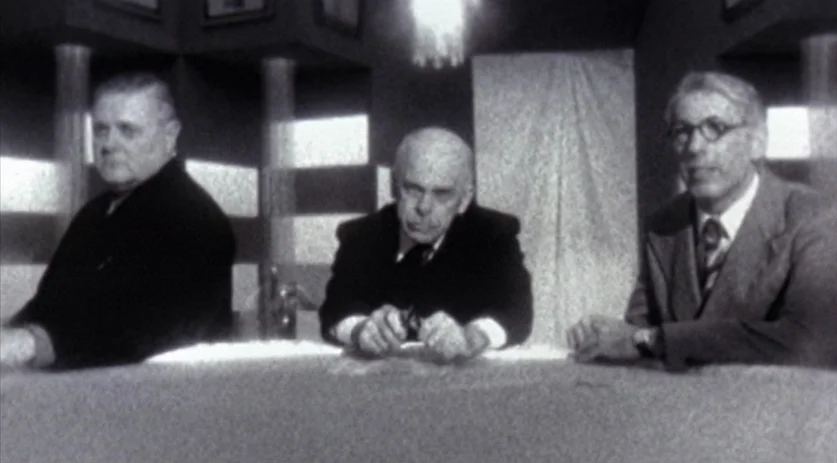 The Saddest Music in the World (2003) movie still: medium — A minimalist studio set features a desk against a backdrop of vertical panels. Three men…