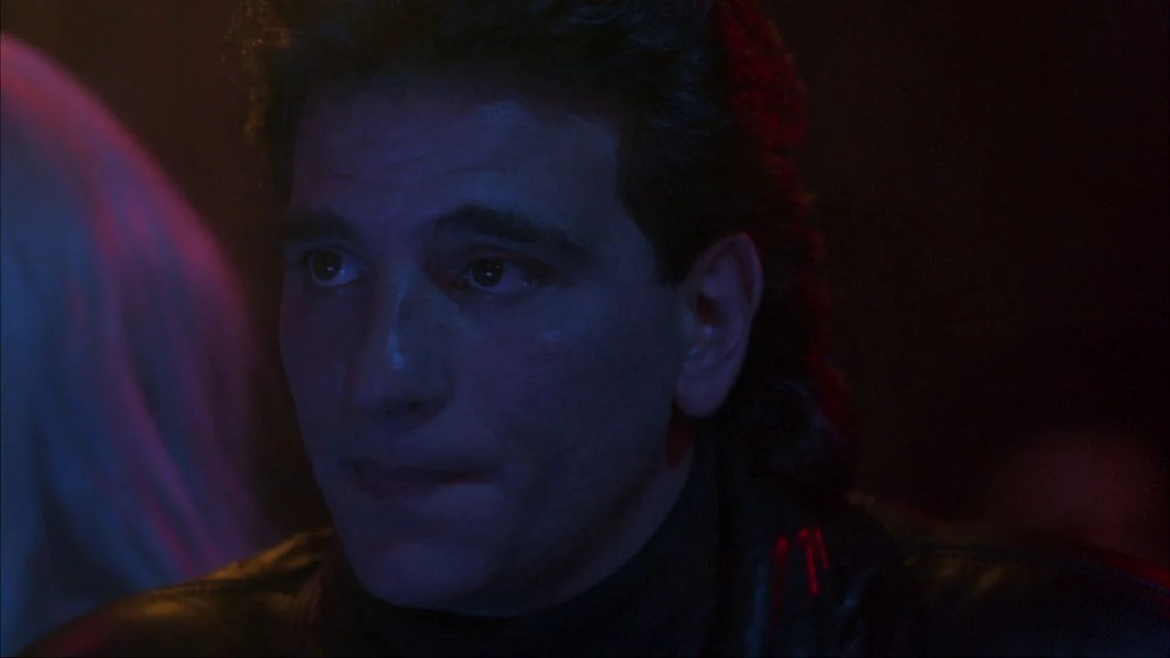 Bad Lieutenant (1992) movie still: closeup — A dark, dimly lit environment with colored light washes against a featureless background. A man with…
