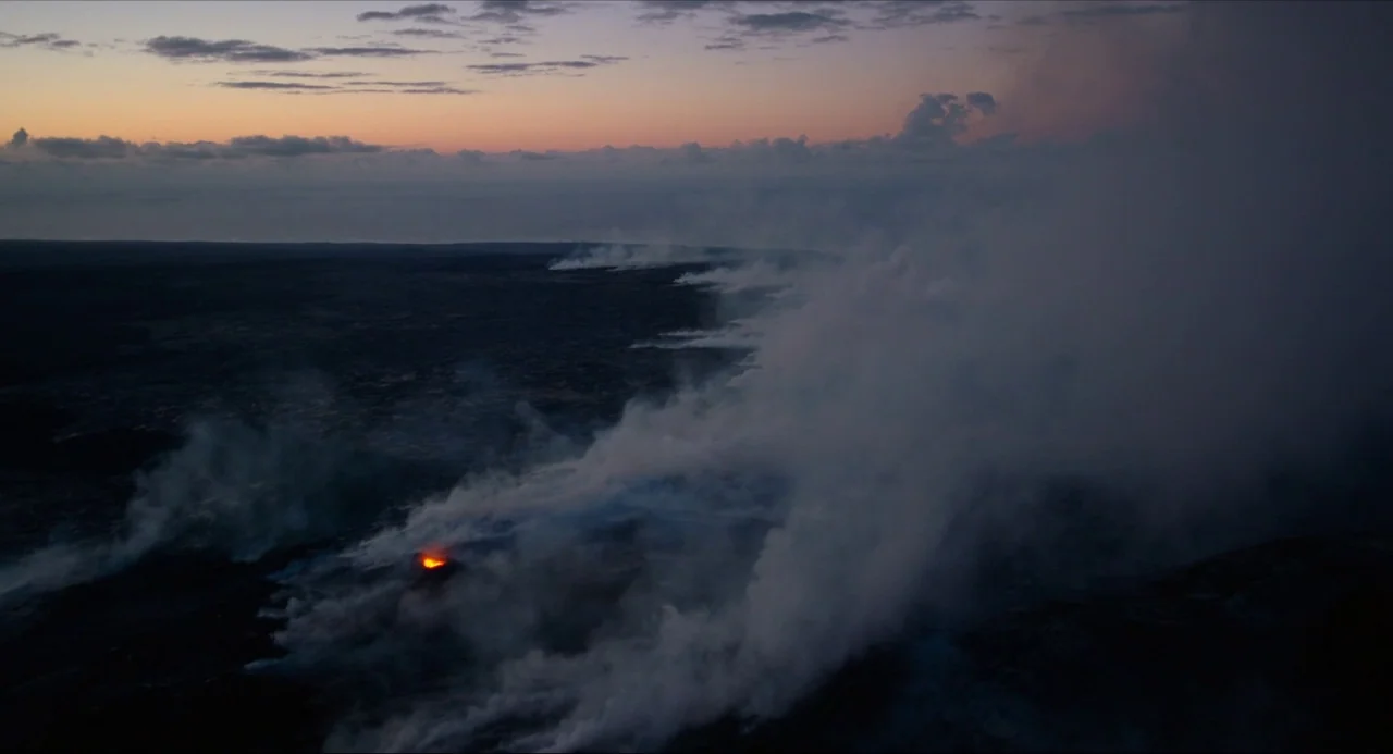 Voyage of Time (2016) movie still: establishing — A dark, expansive volcanic landscape is covered by thick plumes of white volcanic steam. The…