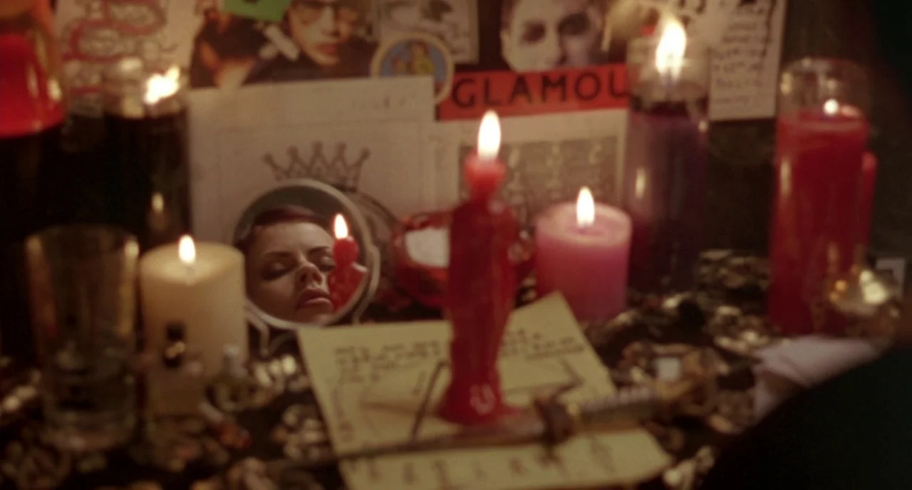 The Craft (1996) movie still: closeup — A cluttered altar surface is covered with lit candles, ritual papers, and small trinkets. A woman's face is…