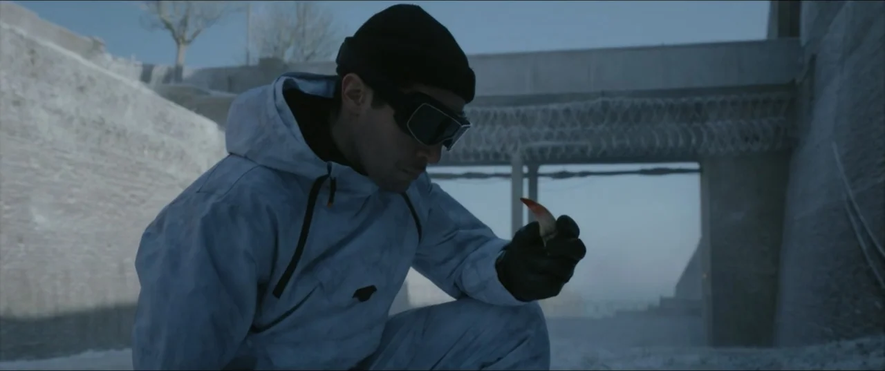 Kraven the Hunter (2024) movie still: medium — A snowy outdoor industrial area features a concrete bridge with coiled barbed wire. A man in a…