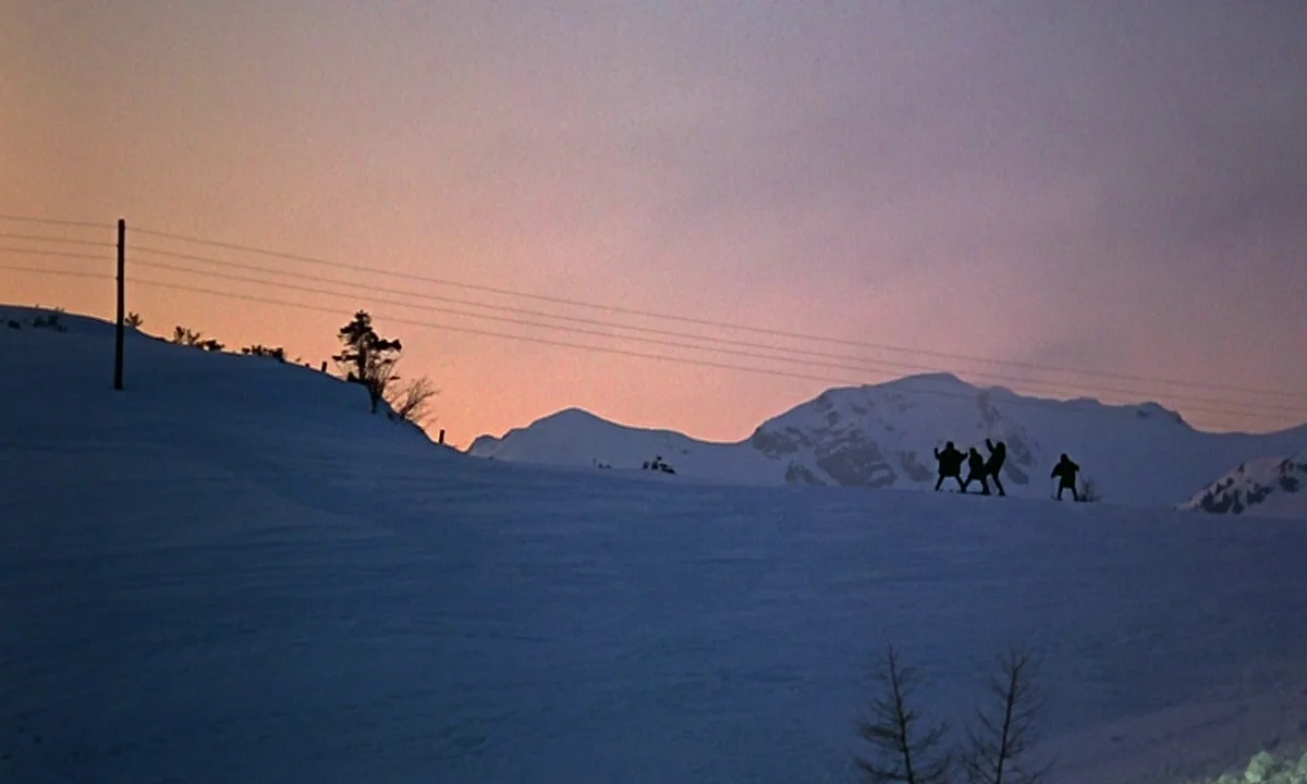 Help! (1965) movie still: wide — A snow-covered mountain slope at dusk features a clear silhouette of four people. Overhead power lines stretch…