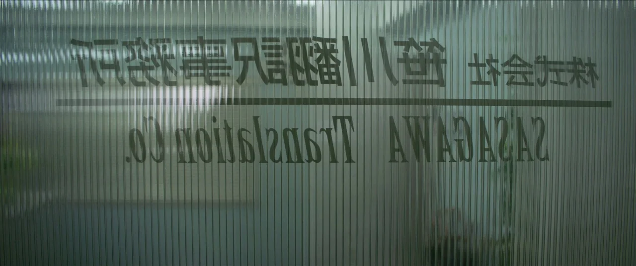 Earthquake Bird movie still: closeup — A ribbed glass panel displays mirrored text for the Sasagawa Translation Company. The background is blurred…