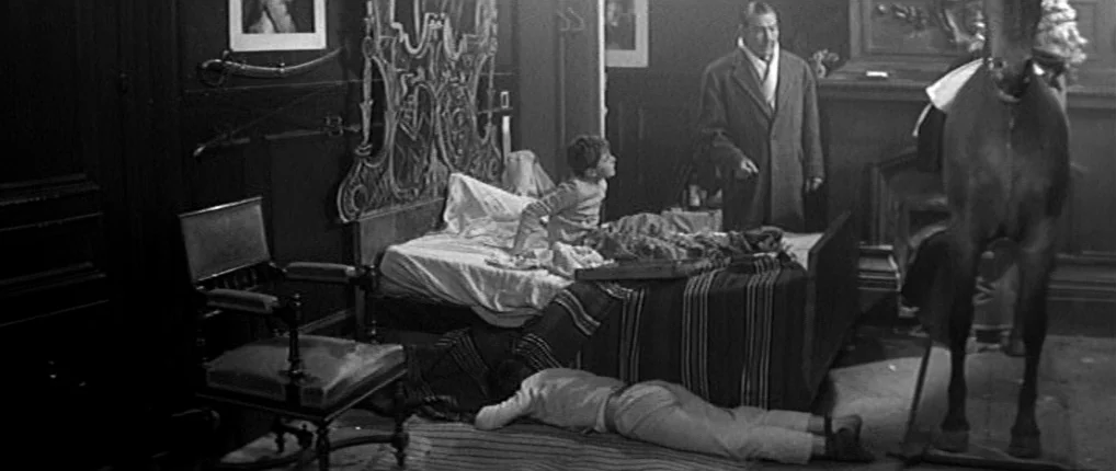 Antoine and Colette (1962) movie still: wide — A dimly lit bedroom features ornate carved wooden furniture and a large equine statue. A man stands…