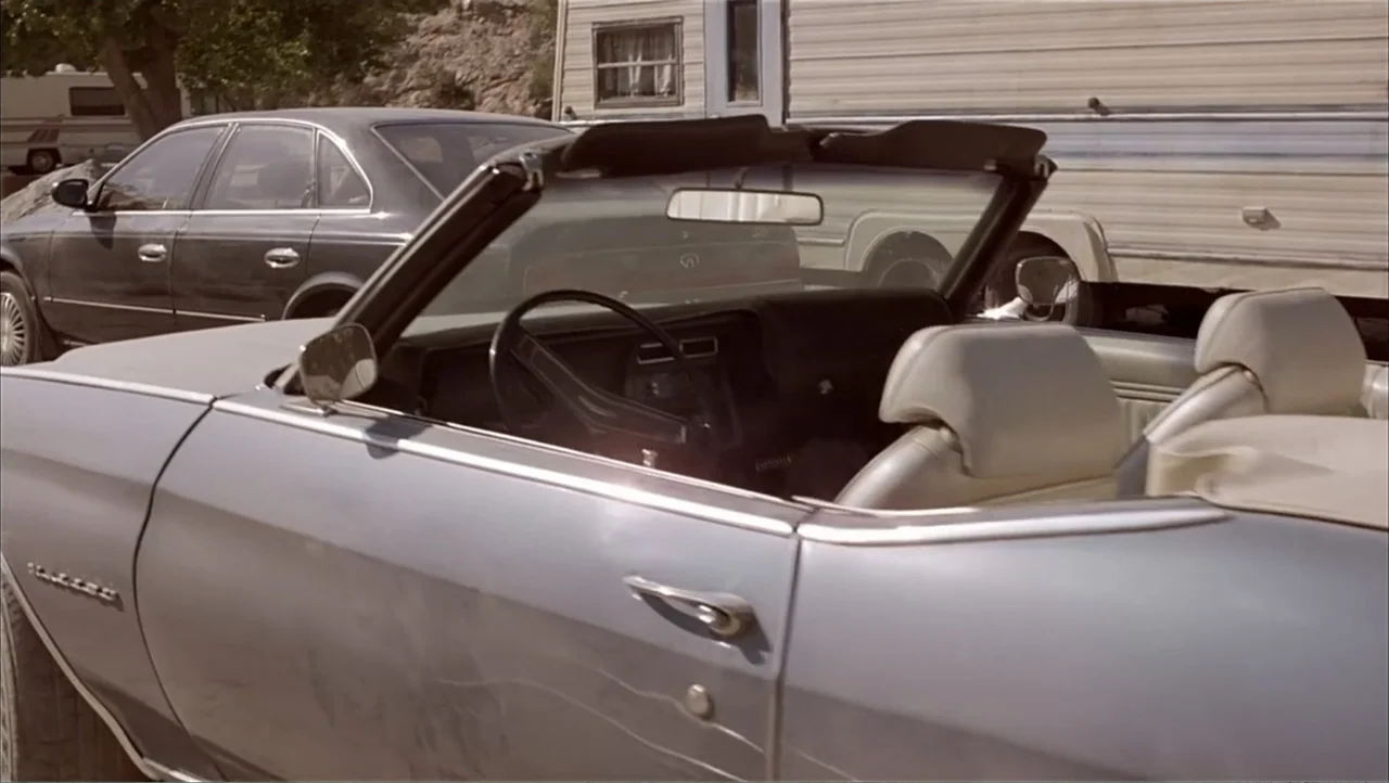 Ajuste de Cuentas (2016) movie still: medium — A silver convertible sits in a dirt lot next to a mobile home. A dark sedan is parked behind the…