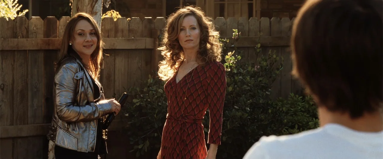 17 Again (2009) movie still: medium — A sunlit wooden fence frames two women standing outside during late afternoon. One woman wears a red patterned…