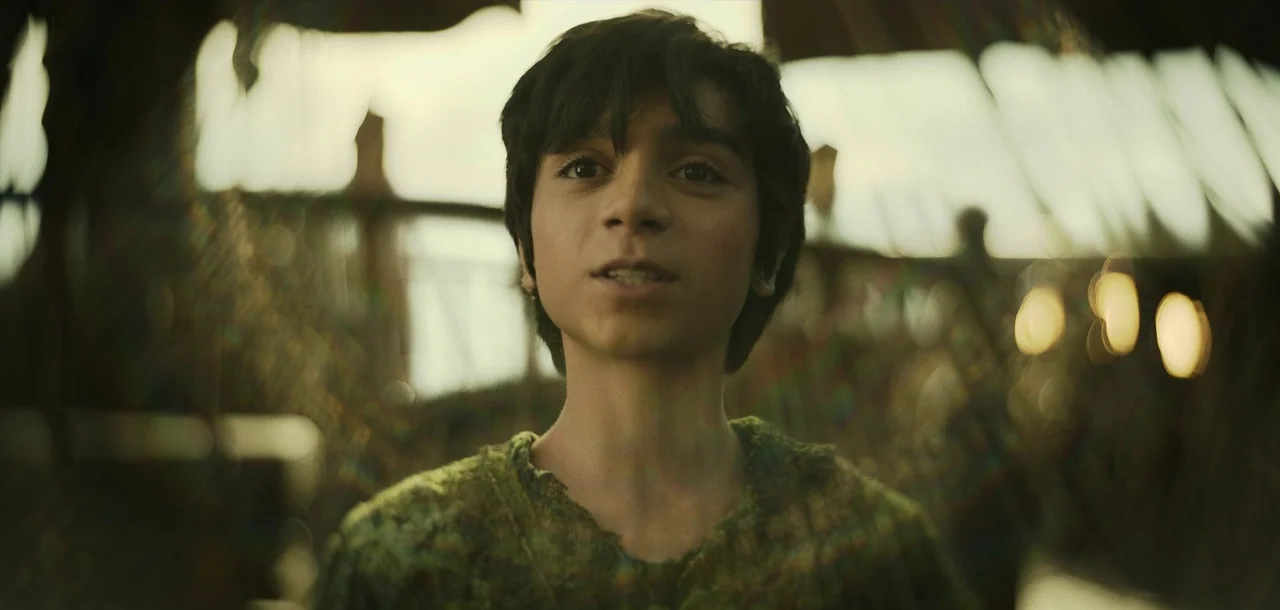 Peter Pan & Wendy (2023) movie still: closeup — A teenage boy stands in a rustic wooden structure with natural light filtering through. He is…