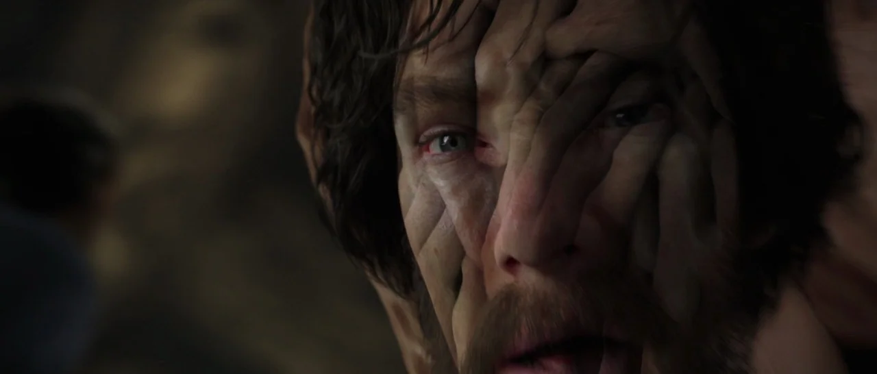 Doctor Strange (2016) movie still: closeup — A man's face is obscured by several layered human hands growing directly from his skin. The dark…