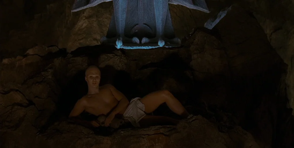 Dominion: Prequel to the Exorcist (2005) movie still: medium — A dark, craggy interior with a large stone statue perched atop a rocky formation. A…