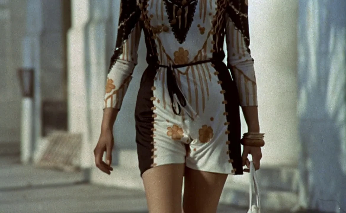 F for Fake (1973) movie still: medium — A woman walks through a stone-pillared colonnade on a clear, sunny day. She is wearing a patterned romper…