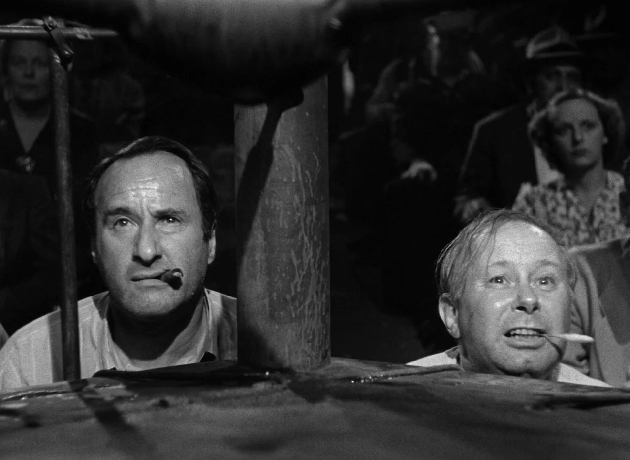 The Set-Up (1949) movie still: medium — Two men sit at the edge of a boxing ring during a dark match. They both stare upward with cigars clenched in…