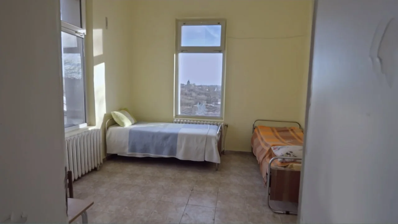 Finding the Way Home (1991) movie still: wide — A spartan hospital room features yellow walls, tiled floors, and two single metal beds. Large…