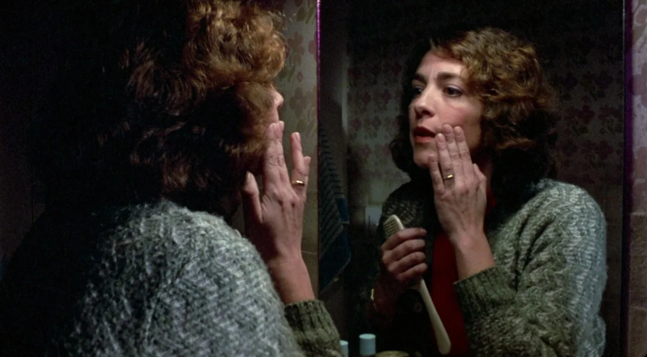 What Have I Done To Deserve This? (1984) movie still: medium — A dimly lit room with floral wallpaper and a large wall-mounted mirror. A woman…