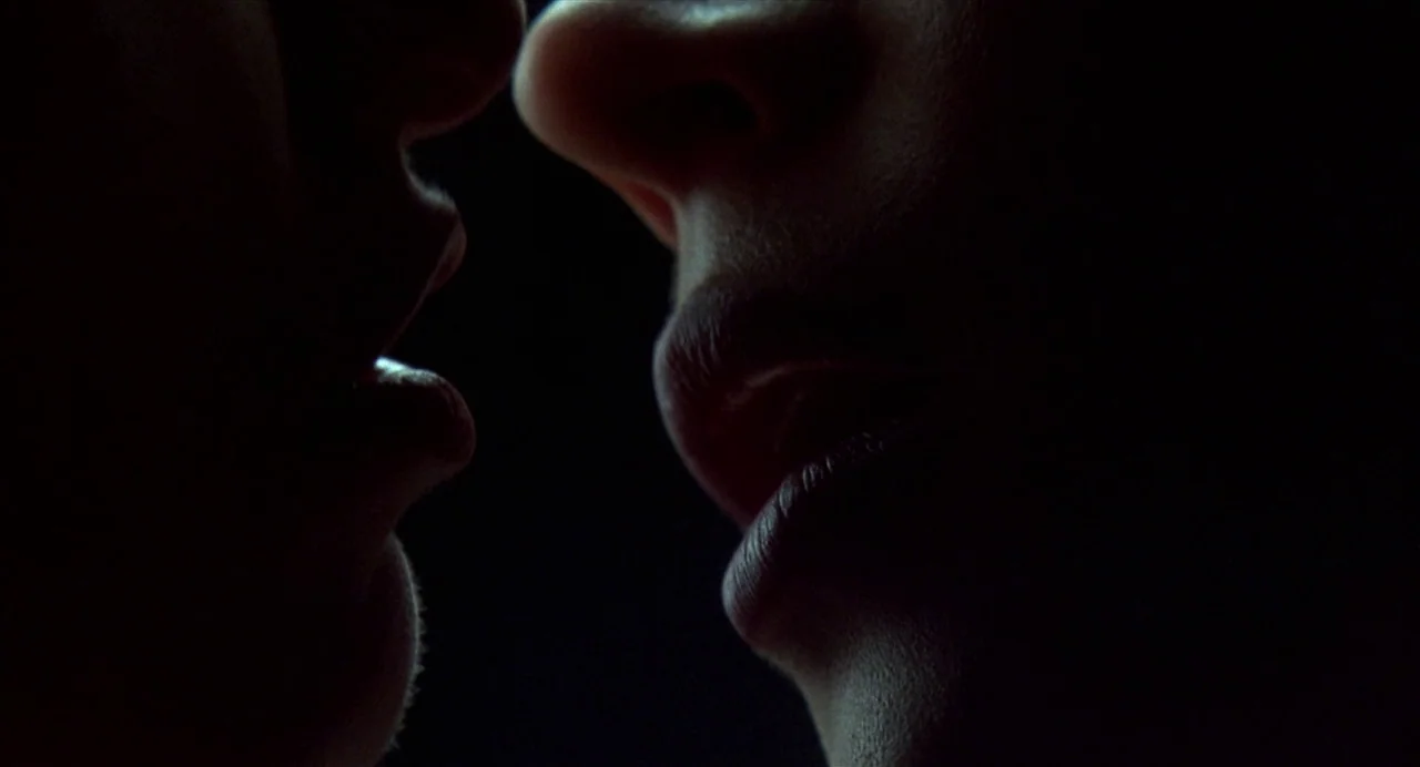 Bound (1996) movie still: closeup — A pitch-black background frames the partial faces of two people in close proximity. The subjects' lips and noses…