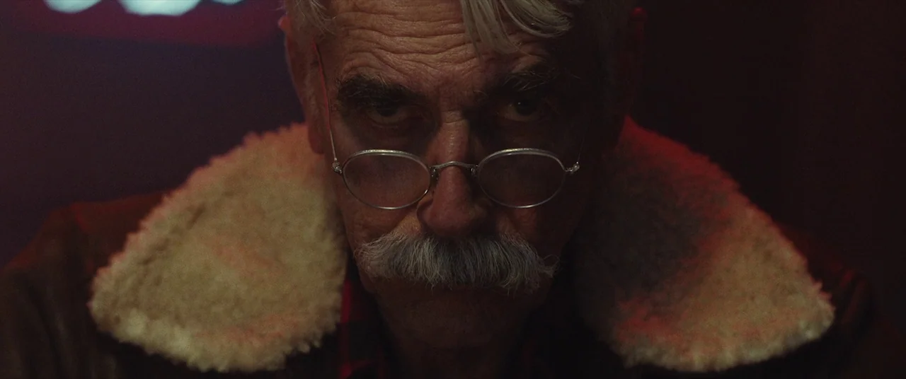 The Man Who Killed Hitler and Then the Bigfoot (2018) movie still: closeup — An elderly man is framed in a dark space lit by red neon light. He…