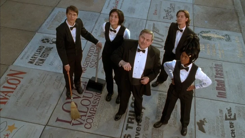 Making of: Castle Freak (1995) movie still: wide — A group of five people in formal attire stand on a patterned paved area. They look directly…
