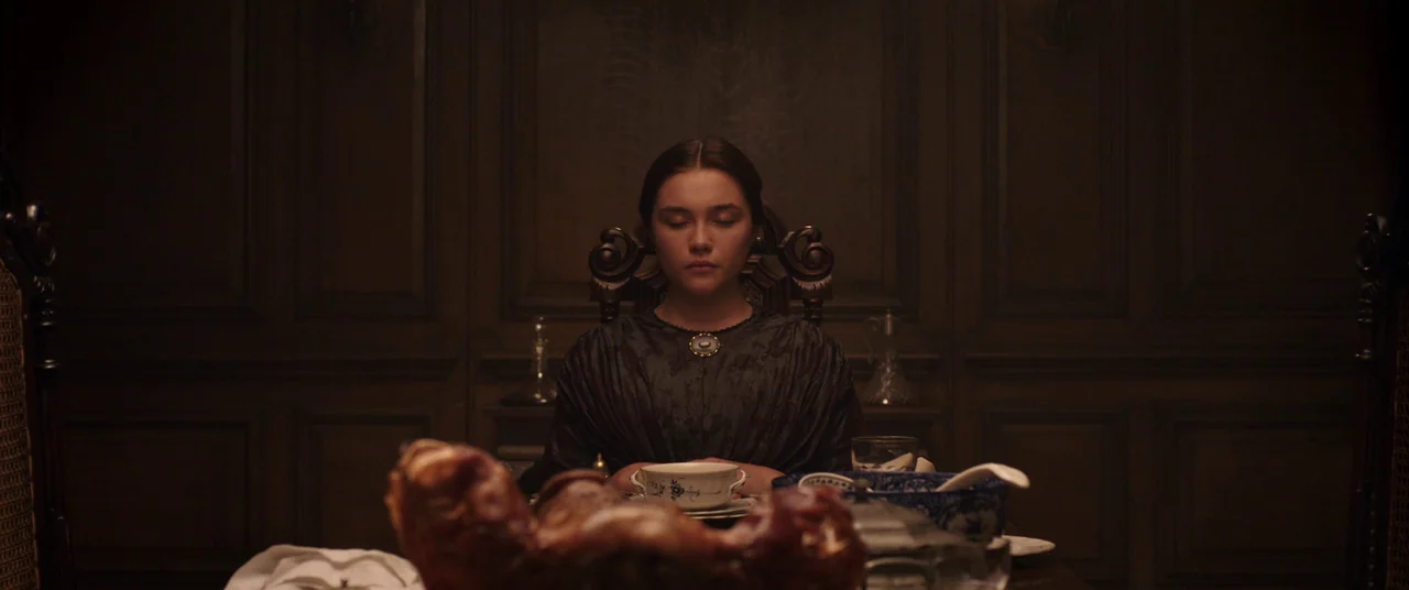Lady Macbeth (2016) movie still: medium — A dark, wood-paneled room features a dining table set with china and food. A woman sits perfectly still at…
