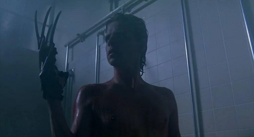 A Nightmare On Elm Street 2: Freddy’s Revenge (1985) movie still: medium — A dimly lit industrial-style shower stall with white square tiles and…