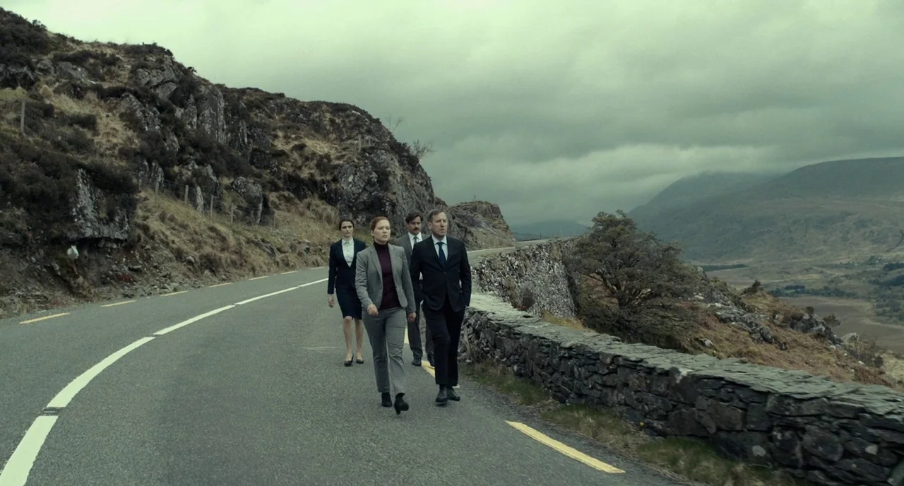 The Lobster (2015) movie still: wide — A desolate, narrow asphalt mountain road winds through a rocky, highland landscape under gray clouds. Four…
