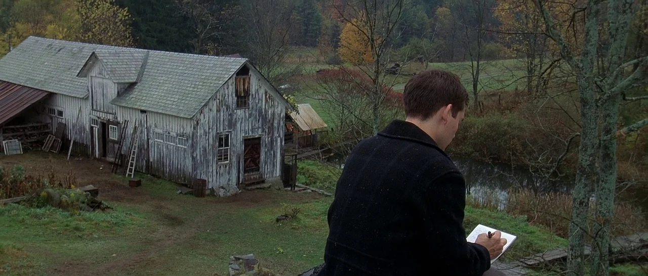 The Cider House Rules movie still: medium — A rural setting features a weathered white barn with graying wooden siding and shingles. A young man…