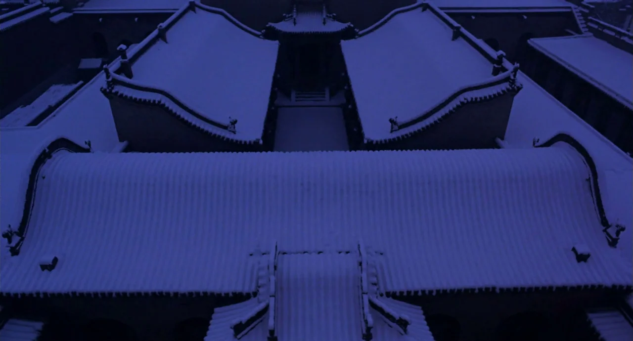 Raise The Red Lantern movie still: establishing — A high-angle view of traditional East Asian tiered roof structures covered in snow. The…