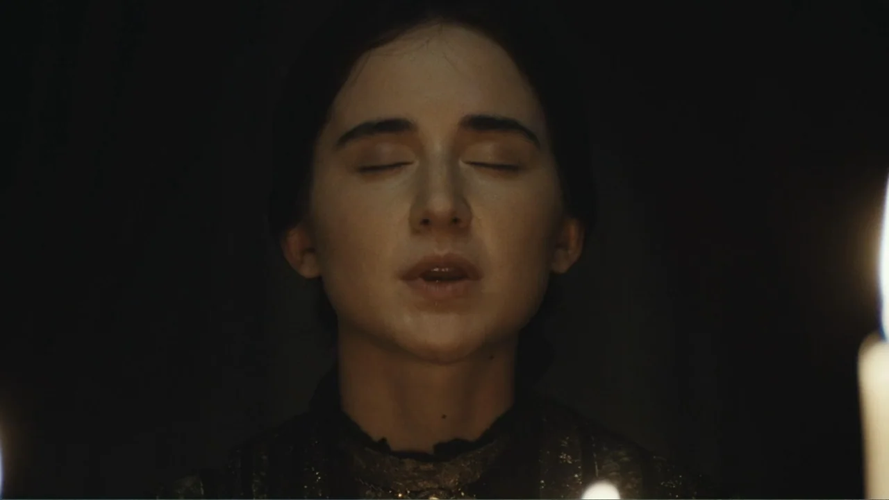 Demon in the White House (2021) movie still: closeup — A dark, dimly lit interior space features a woman in period clothing. She stands with her…
