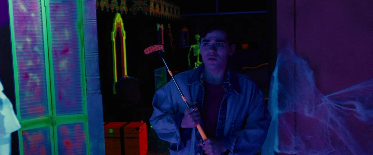 Freaky (2020) movie still: medium — A dimly lit miniature golf course environment glows under ultraviolet lights with cobweb decorations. A young…