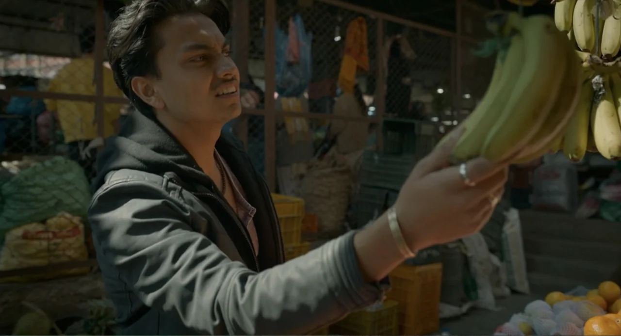 Ice Road: Vengeance (2025) movie still: medium — An outdoor market stall features wire fencing, stacked plastic crates, and diverse produce. A young…