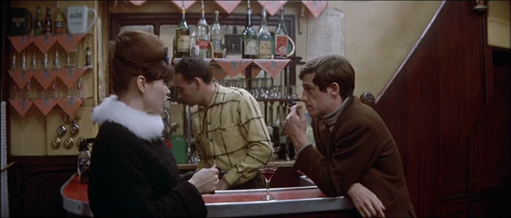 Une Femme Est Une Femme (A Woman Is a Woman) (1961) movie still: medium — A dimly lit European style bar interior features shelves lined with liquor…
