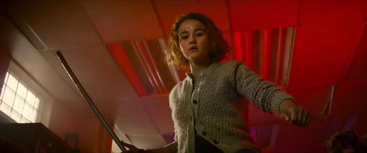A Quiet Place Part II (2020) movie still: medium — An office interior with a drop-ceiling is illuminated by a deep red emergency light. A young…