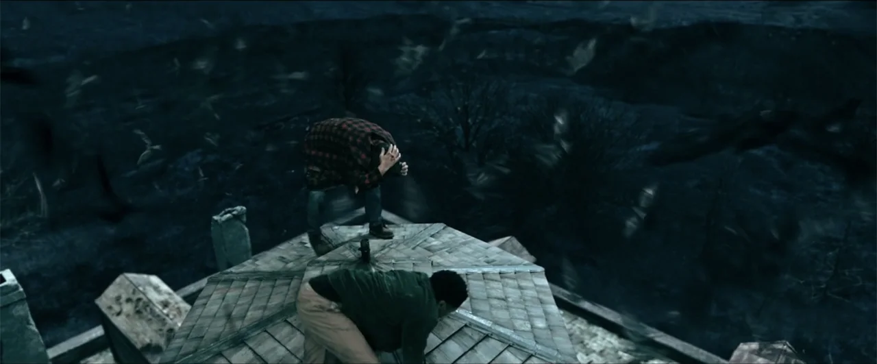Jeepers Creepers: Reborn (2022) movie still: wide — Two men crouch on the peak of a steep, shingled roof at night. A large flock of birds swirls…