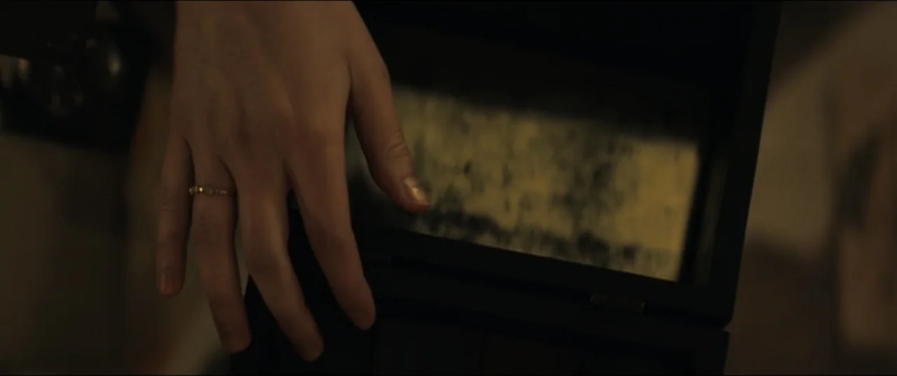 Vicious (2025) movie still: closeup — A close overhead view shows a hand resting on the rim of a box. The interior of the box contains textured…