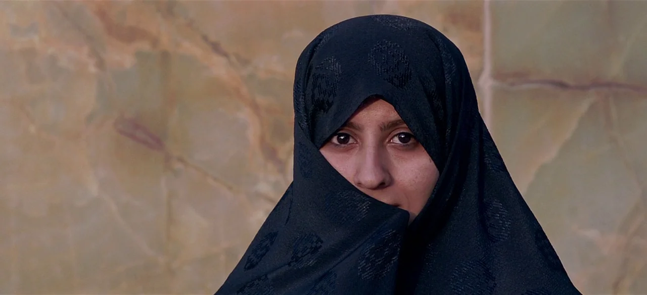 Baraka (1992) movie still: closeup — A person stands before a smooth slab of polished olive-colored marble stone. A woman wearing a black headscarf…
