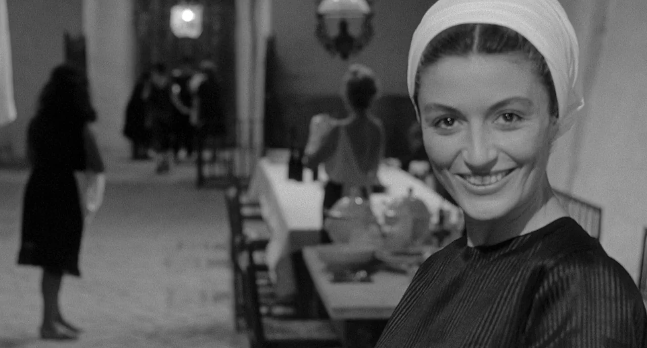 8 1/2 (1963) movie still: closeup — A spacious stone-floored dining hall features a long table set with various dinnerware items. A woman in the…