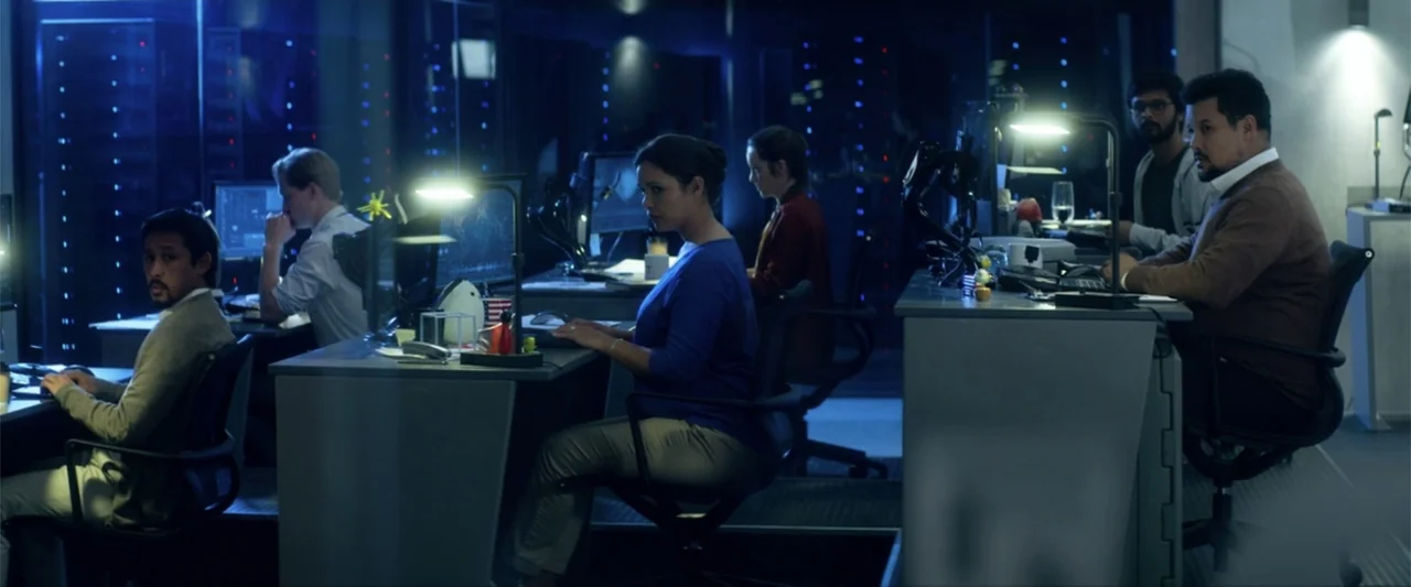 Bloodshot (2020) movie still: wide — A modern, dimly lit office space contains multiple rows of server racks and workstations. Five people work…