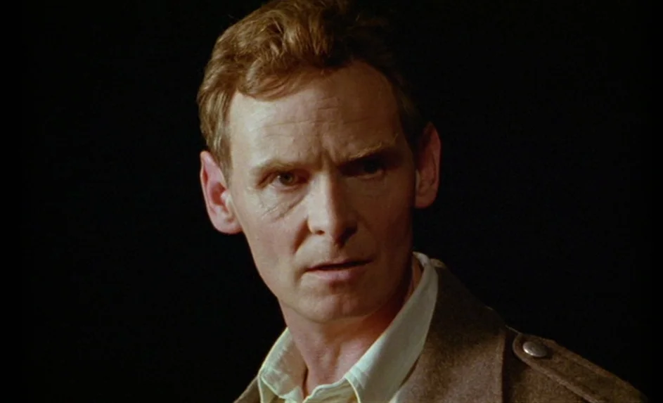 Wittgenstein (1993) movie still: closeup — A dimly lit, featureless dark environment surrounds a man's upper torso and head. The man looks toward…