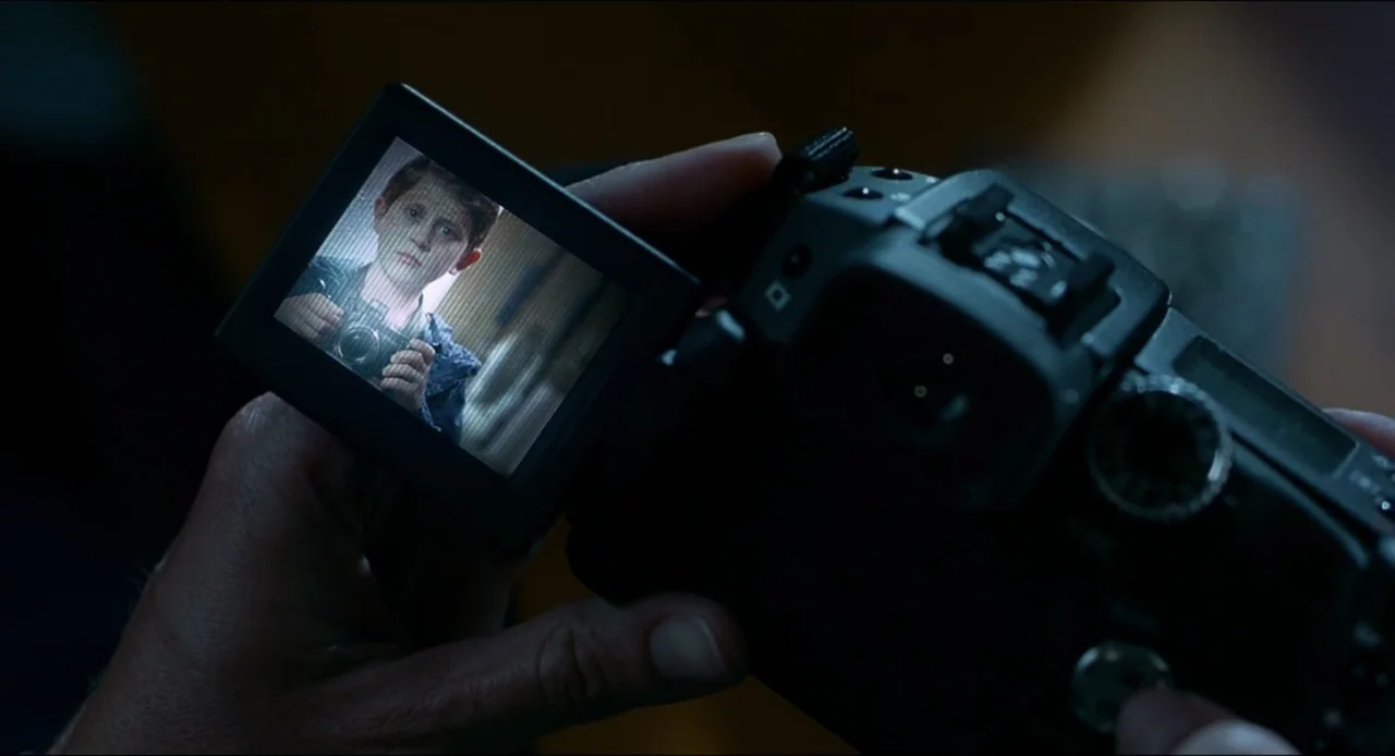 The Ring Two (2005) movie still: closeup — A close-up view shows a hand holding a digital camera with an open LCD screen. The screen displays a…
