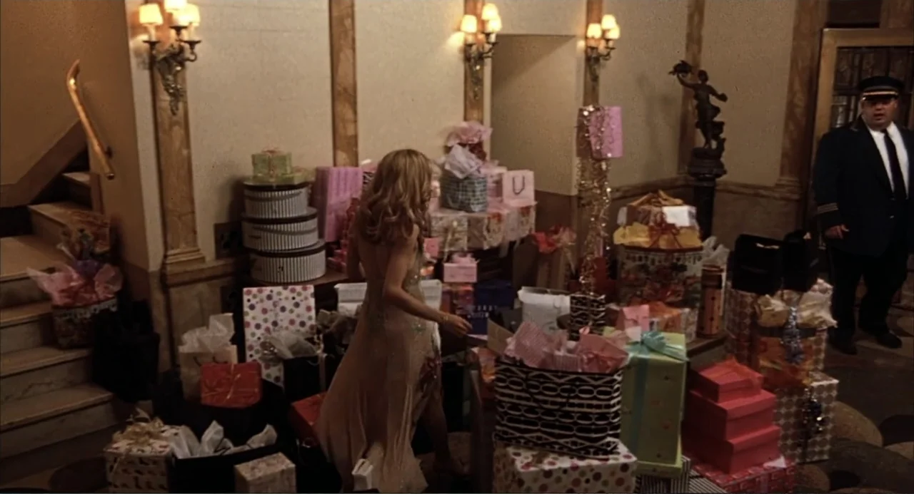 Uptown Girls (2003) movie still: medium — An opulent apartment building lobby filled with dozens of gift-wrapped packages. A woman in a gown stands…