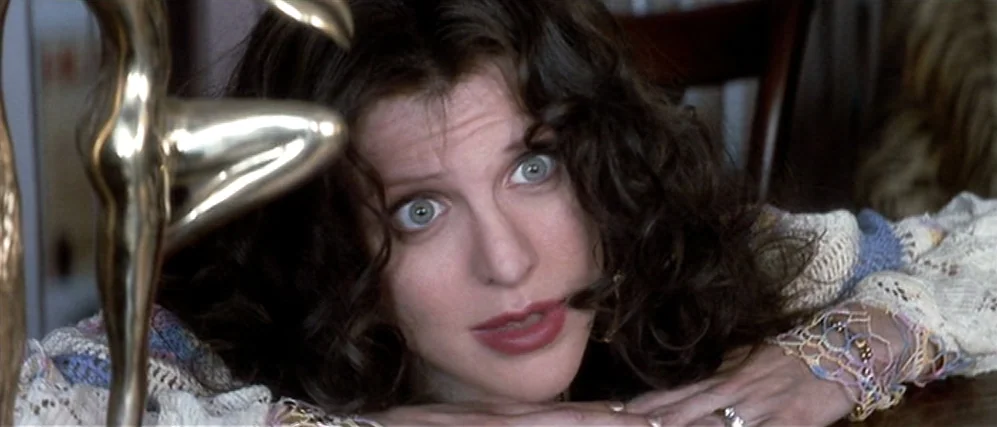 The People vs. Larry Flint (1996) movie still: closeup — A woman rests her chin on her hands while looking at the camera. A polished metal figurine…