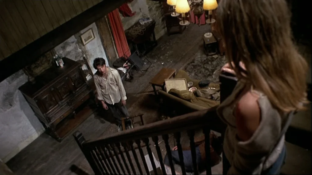 Straw Dogs (1971) movie still: medium — A rustic cottage interior features exposed stone walls and dark wooden floorboards. A disheveled man stands…