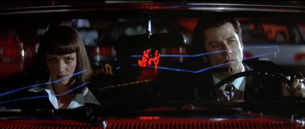 Pulp Fiction (1994) movie still: medium — A dark car interior at night features a red dashboard display reflected on the windshield. A man drives…