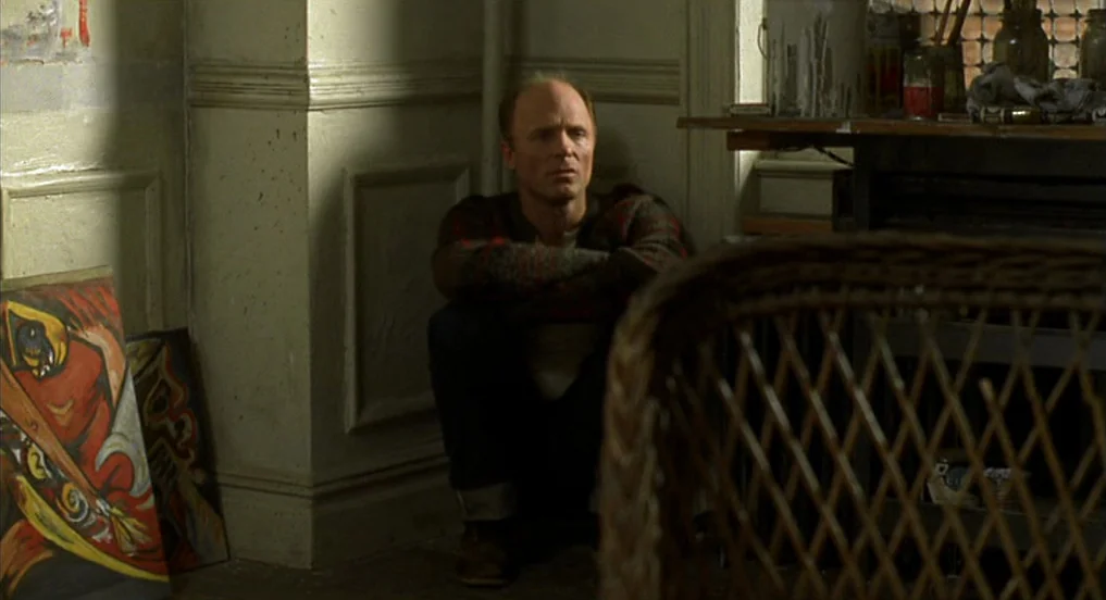 Pollock (2000) movie still: medium — A corner of a room features white wainscoting and nearby abstract paintings on the floor. A man sits against…