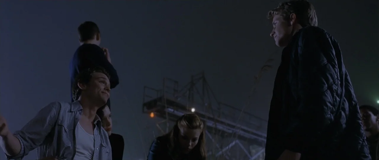 A Walk to Remember (2002) movie still: medium — An industrial lot at night with a metal structure visible in the background. A group of five young…